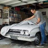man putting cover on white classic car in garage. 